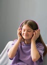 A teenager girl in a lilac T-shirt in pink headphones listens to audio music, emotions of teenager.