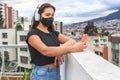 Teenager girl with a mask listening to music with wireless headphones and taking a selfie with her cell phone on a terrace or Royalty Free Stock Photo