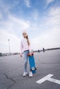 A teenager girl in a pink hat and jeans stands with a pennyboard. Royalty Free Stock Photo