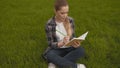 Teenager girl in a plaid shirt sits on the grass and takes notes in a notebook. 4K