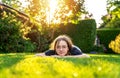 Teenager girl relaxing lying on green grass in garden backyard at sunset with backlit. Royalty Free Stock Photo