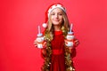 Teenager girl in Santa hat and tinsel on the neck, holds 2 bottles of juice Christmas in the shape of a snowman on a red