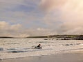 Teenager girl on a surf board in a waves. Blackrock diving tower in the background. Beautiful cloudy sky, Galway city, Ireland. Royalty Free Stock Photo