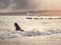 Teenager girl on a surf board in a waves. Blackrock diving tower in the background. Beautiful cloudy sky, Galway city, Ireland. Royalty Free Stock Photo