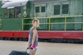 Teenager girl at the train station near the locomotive. girl pulling a large suitcase on the platform Royalty Free Stock Photo