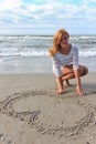 Teenager girl in a white dress draw heart on sand