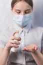 Teenager girl of 11-14 years old, in medical mask covers face, holds an antiseptic spray in hand, disinfects hands from