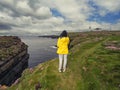 Teenager girl in yellow jacket on edge of stunning cliff in county Clare, Ireland, Loop head area. Dramatic cloudy sky. Irish Royalty Free Stock Photo
