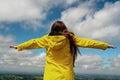 Teenager girl in yellow jacket with hands up in the air. White cloudy sky background. Positive body language. Copy space