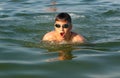 Teenager in goggles swims in the sea with big splashes. Cute boy enjoys swimming in the ocean. Royalty Free Stock Photo