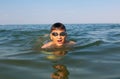 Teenager in goggles swims in the sea with big splashes. Cute boy enjoys swimming in the ocean. Royalty Free Stock Photo