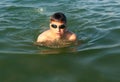 Teenager in goggles swims in the sea with big splashes. Cute boy enjoys swimming in the ocean. Royalty Free Stock Photo