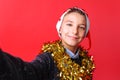 A teenager guy takes a selfie in a Santa hat and tinsel on the neck, on a red background