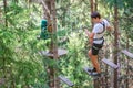 Teenager having fun on high ropes course, adventure park, climbing trees in a forest in summer Royalty Free Stock Photo
