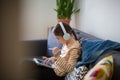 Teenager with headphones is sitting on sofa and study. student girl with tablet in room at home