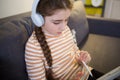 Teenager with headphones is sitting on sofa and study. student girl with tablet in room at home