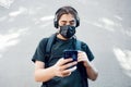 Teenager high school boy with medical mask, headphones and backpack, texting with his mobile smart phone Royalty Free Stock Photo