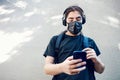 Teenager high school boy with medical mask, headphones and backpack, texting with his mobile smart phone Royalty Free Stock Photo