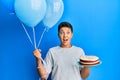 Teenager hispanic boy celebrating birthday with cake holding balloons celebrating crazy and amazed for success with open eyes Royalty Free Stock Photo