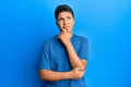 Teenager hispanic boy wearing casual blue t shirt thinking concentrated about doubt with finger on chin and looking up wondering