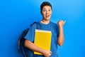 Teenager hispanic boy wearing school bag and holding books pointing thumb up to the side smiling happy with open mouth Royalty Free Stock Photo