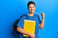 Teenager hispanic boy wearing school bag and holding books screaming proud, celebrating victory and success very excited with Royalty Free Stock Photo