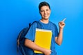 Teenager hispanic boy wearing school bag and holding books smiling happy pointing with hand and finger to the side Royalty Free Stock Photo