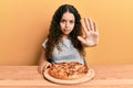 Teenager hispanic girl eating italian pizza with open hand doing stop sign with serious and confident expression, defense gesture Royalty Free Stock Photo