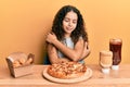 Teenager hispanic girl eating pizza and fried chicken hugging oneself happy and positive, smiling confident Royalty Free Stock Photo