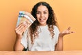 Teenager hispanic girl holding canadian dollars celebrating achievement with happy smile and winner expression with raised hand