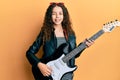 Teenager hispanic girl playing electric guitar winking looking at the camera with sexy expression, cheerful and happy face