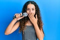 Teenager hispanic girl singing song using microphone covering mouth with hand, shocked and afraid for mistake Royalty Free Stock Photo