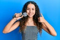 Teenager hispanic girl singing song using microphone smiling happy and positive, thumb up doing excellent and approval sign Royalty Free Stock Photo