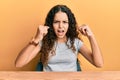 Teenager hispanic girl wearing casual clothes sitting on the table angry and mad raising fists frustrated and furious while