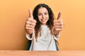 Teenager hispanic girl wearing casual clothes sitting on the table approving doing positive gesture with hand, thumbs up smiling Royalty Free Stock Photo