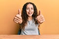 Teenager hispanic girl wearing casual clothes sitting on the table approving doing positive gesture with hand, thumbs up smiling Royalty Free Stock Photo
