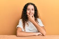 Teenager hispanic girl wearing casual clothes sitting on the table looking confident at the camera smiling with crossed arms and Royalty Free Stock Photo