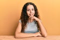 Teenager hispanic girl wearing casual clothes sitting on the table looking confident at the camera smiling with crossed arms and Royalty Free Stock Photo