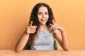 Teenager hispanic girl wearing casual clothes sitting on the table pointing fingers to camera with happy and funny face Royalty Free Stock Photo