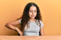 Teenager hispanic girl wearing casual clothes sitting on the table suffering of backache, touching back with hand, muscular pain Royalty Free Stock Photo