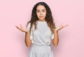 Teenager hispanic girl wearing casual white t shirt clueless and confused expression with arms and hands raised