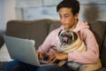 Teenager at home working with his laptop on the sofa with a pug next to him - best friends on the sofa hugged together