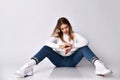 Teenager in jeans, sweater, socks and sneakers. She looking at her watch sitting on floor, legs apart,  on white. Close up Royalty Free Stock Photo