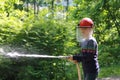 Teenager learning the firefighter profession. The girl in fire helmet pours water from the hose