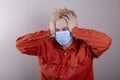 A teenager in a medical mask holds his head against a gray background.Headache for juvenile delinquents in quarantine, criminal li Royalty Free Stock Photo