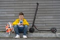 Teenager with mobile phone sitting next to his electric scooter and backpack. Modern young boy chatting on smartphone. Royalty Free Stock Photo