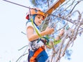 Teenager in orange helmet climbing in trees on forest adventure park