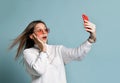 Teenager in orange sunglasses, watch, bracelet and sweater. She taking selfie, surprised, posing on blue background. Close up Royalty Free Stock Photo
