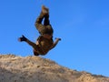 Teenager performs freerunning somersault on sand hill