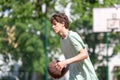 Teenager playing basketball smiling, cheerful. Fit boy with basketball ball outdoors. Kid dribbling the ball at the court